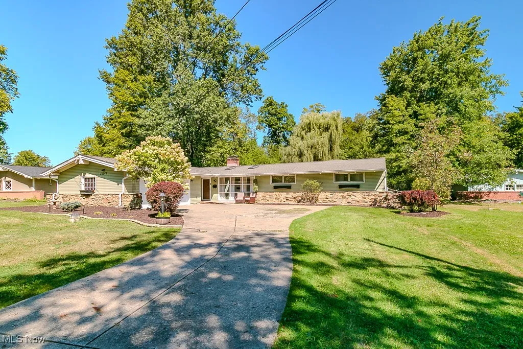 Ranch-style house with a chimney, concrete driveway, a front lawn, and stone siding