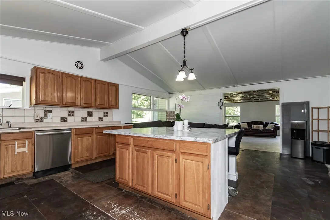 Kitchen featuring brown cabinets, tasteful backsplash, light countertops, stainless steel dishwasher, and hanging light fixtures