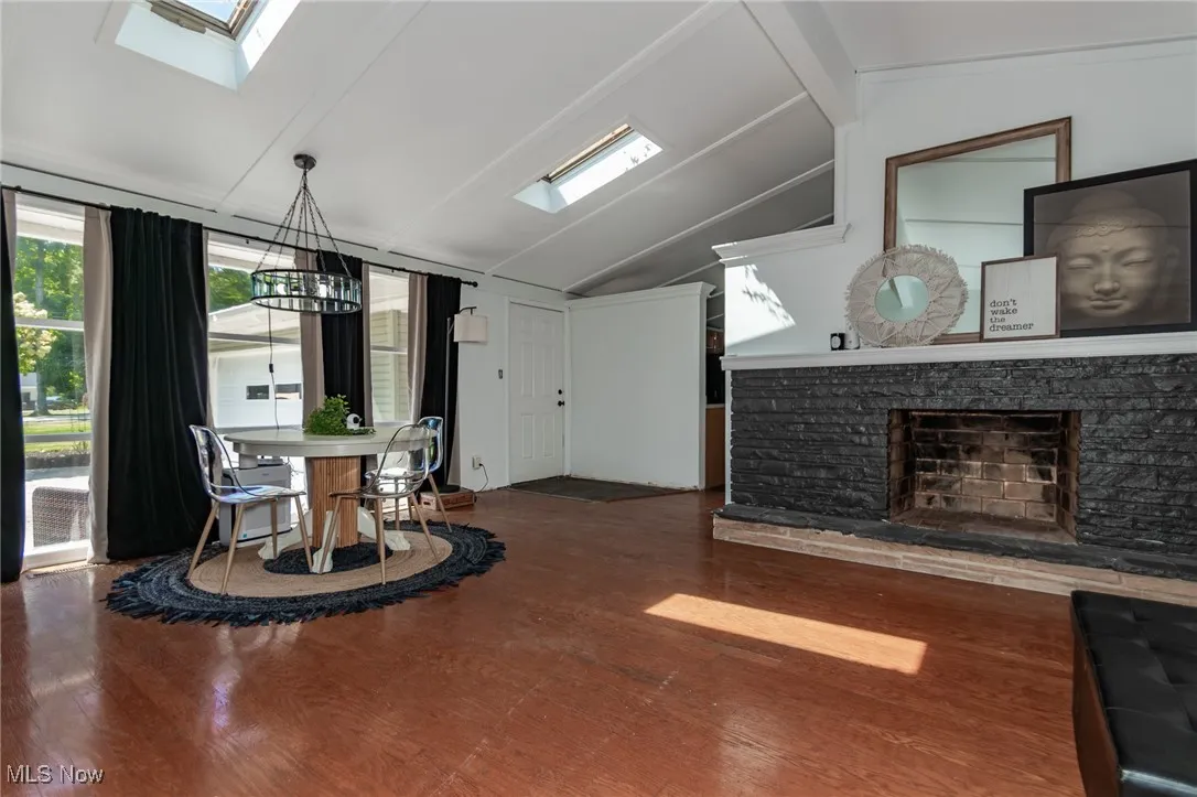 Dining area with a skylight, wood finished floors, a chandelier, and a stone fireplace