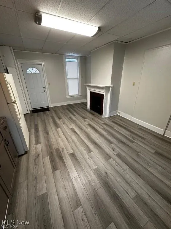 Unfurnished living room with a drop ceiling, a fireplace, and light wood-style floors