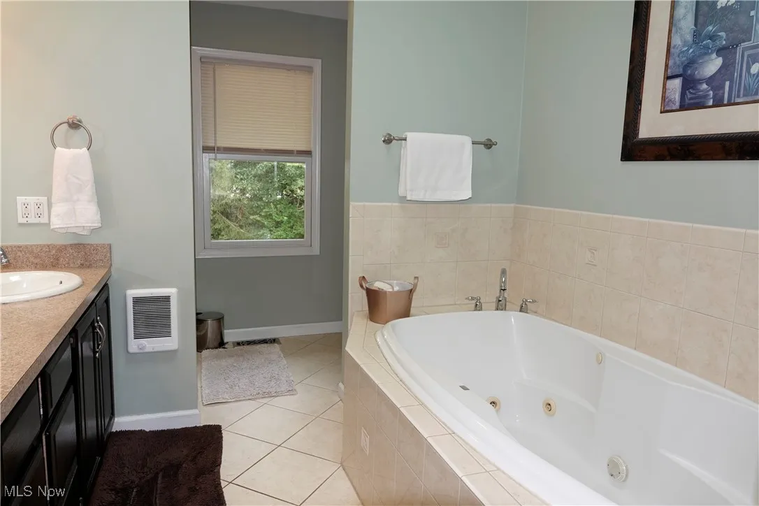 Bathroom with vanity, a tub with jets, light tile patterned floors, and heating unit