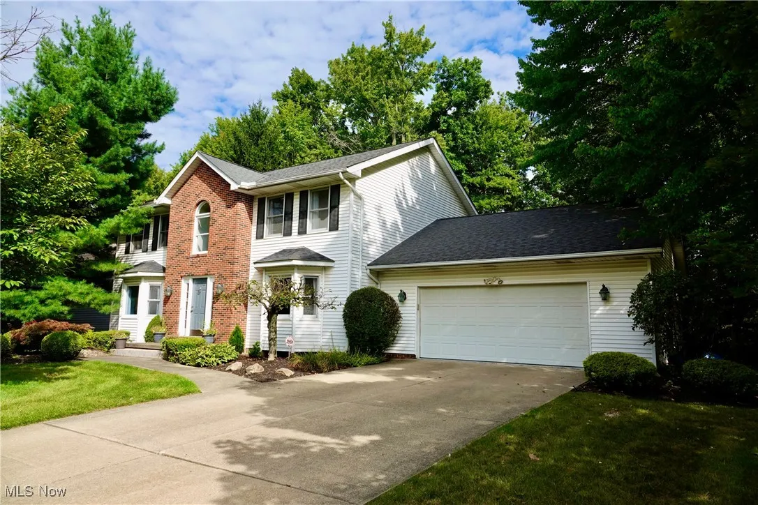 Colonial house featuring driveway, a garage, roof with shingles, a balcony, and a front yard