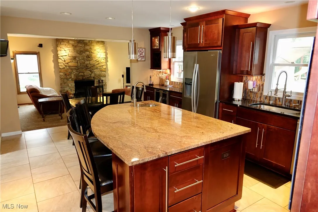 Kitchen with a kitchen bar, dark stone countertops, open floor plan, stainless steel refrigerator with ice dispenser, and dark brown cabinets
