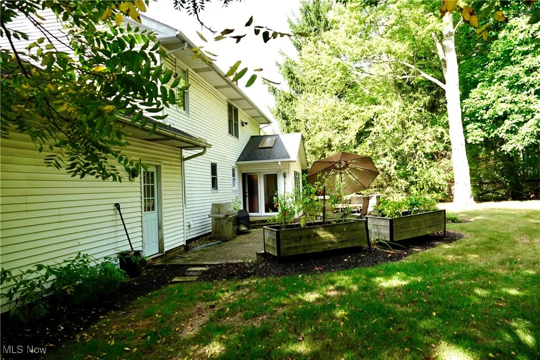 View of grassy yard with a patio, a garden, a deck, and view of wooded area