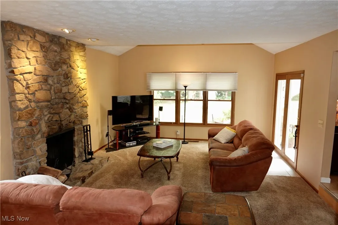 Living room with vaulted ceiling, a stone fireplace, a textured ceiling, and carpet