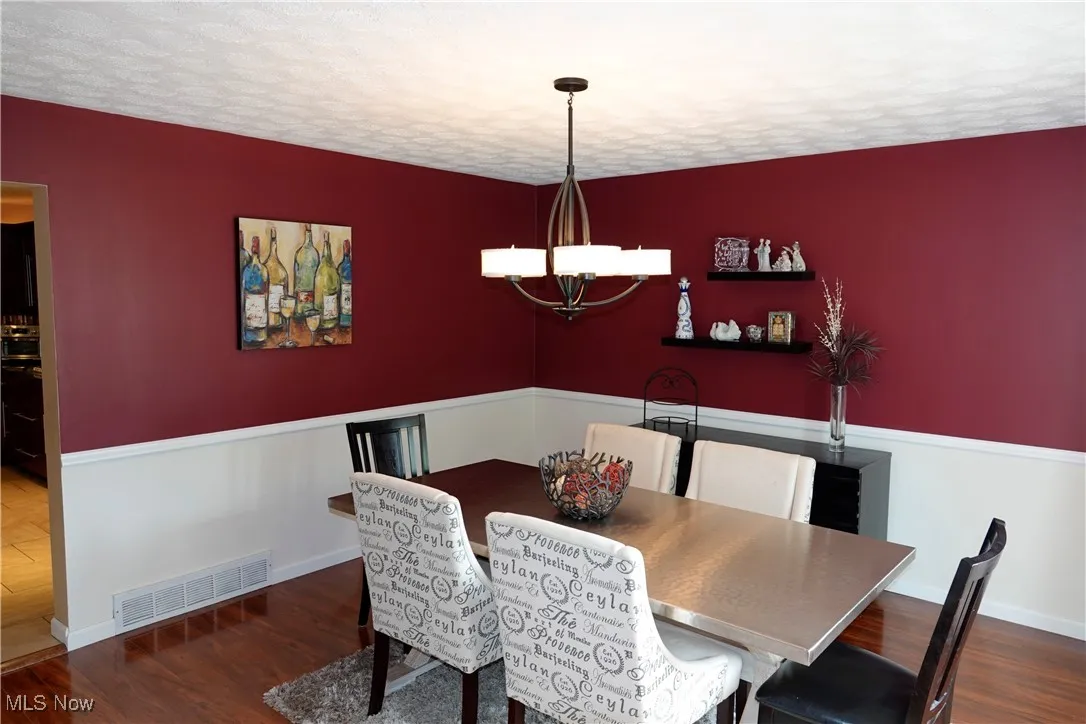Dining area featuring dark wood-type flooring, a textured ceiling, and a chandelier