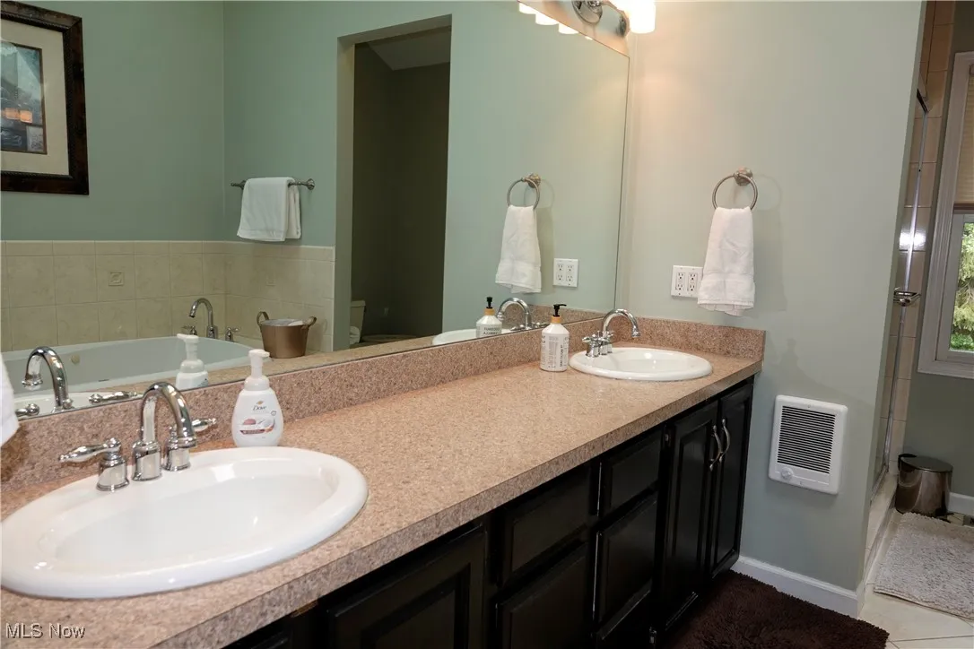 Full bathroom featuring a shower stall, double vanity, a garden tub, heating unit, and tile patterned floors