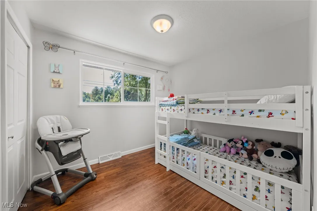 Bedroom with dark wood-type flooring, a closet, and a crib