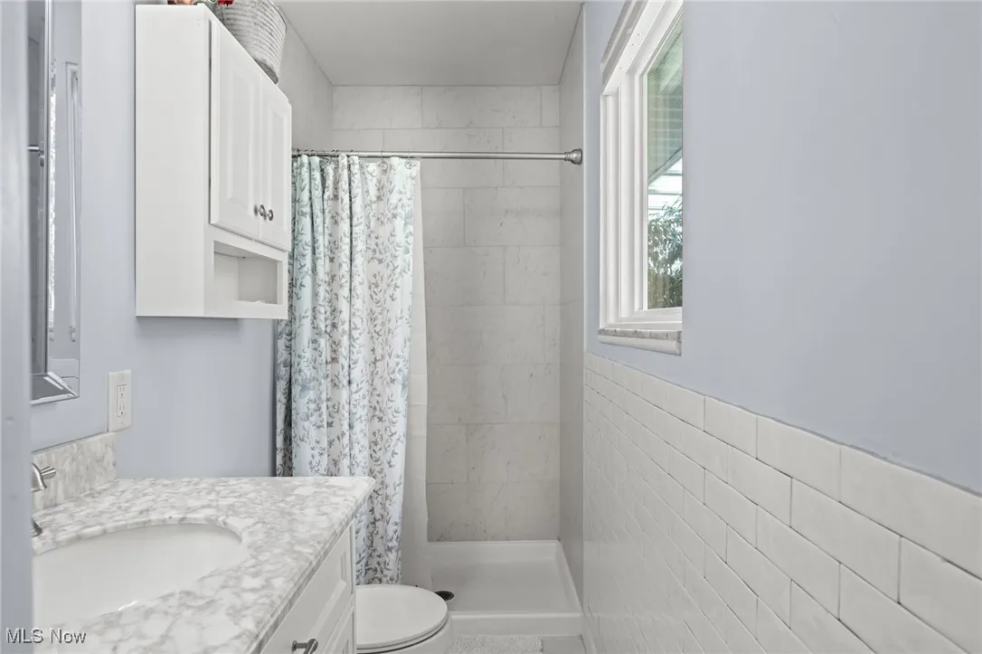 Full bathroom with a stall shower, vanity, and tile walls