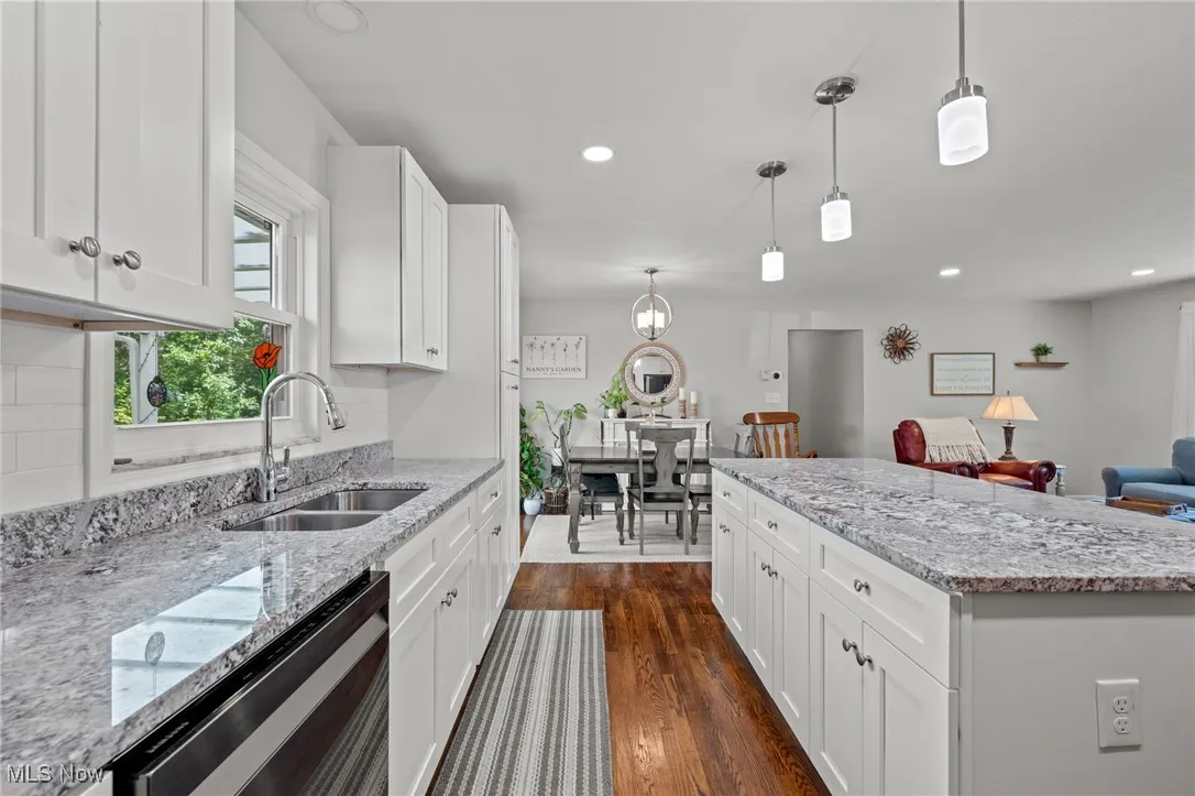 Kitchen featuring white cabinetry, light stone countertops, dark wood-type flooring, decorative light fixtures, and stainless steel dishwasher