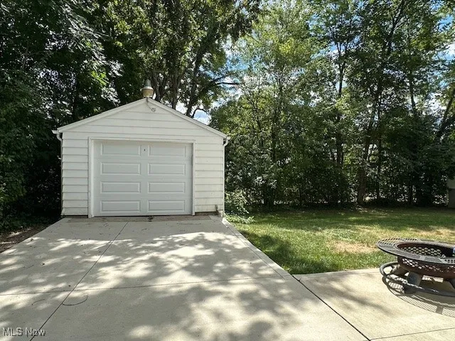 Detached garage featuring concrete driveway and view of wooded area