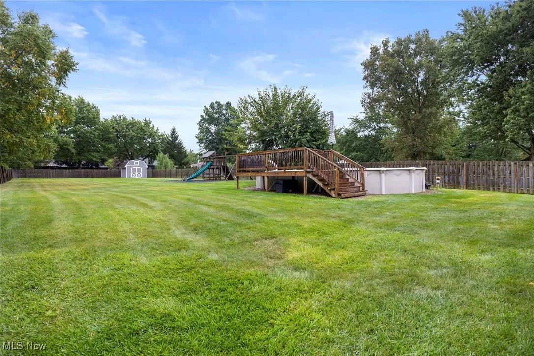 Fenced backyard with a shed, a playground, an outdoor pool, stairs, and a wooden deck