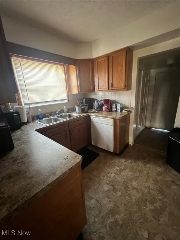 Kitchen with brown cabinets, dishwasher, light countertops, dark stone finish floors, and a textured ceiling