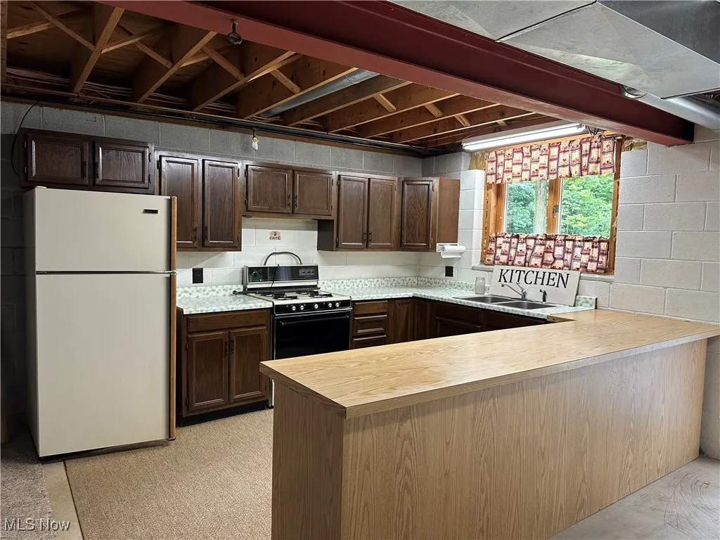 Downstairs Kitchen with light countertops, freestanding refrigerator, gas range oven, a peninsula, and dark brown cabinets