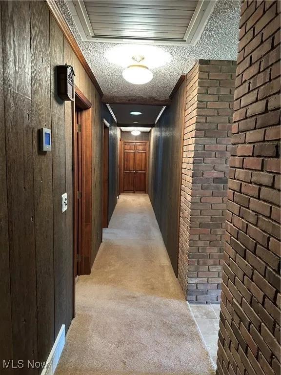 Corridor with light carpet, cooling unit, wooden walls, and crown molding