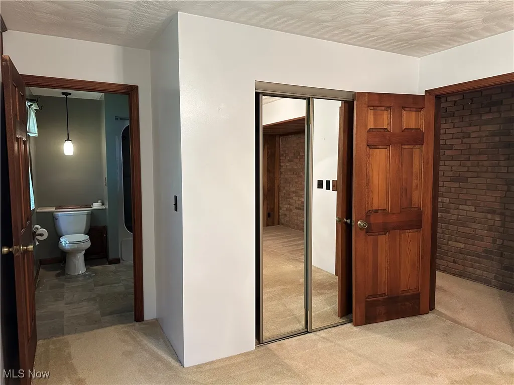 Bedroom with light carpet, a closet, brick wall, and connected bathroom