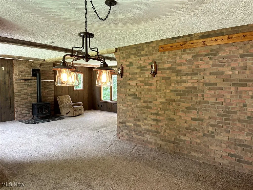 Dining room, living room featuring brick wall, a wood stove, a textured ceiling, carpet, and beam ceiling