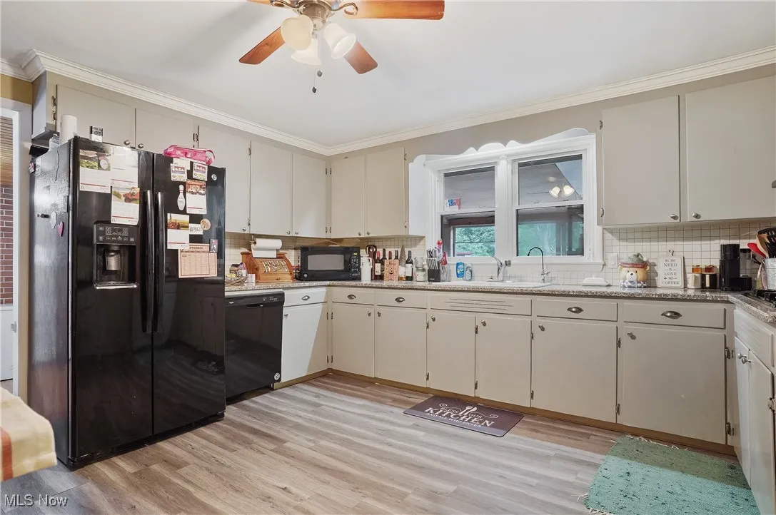 Kitchen featuring black appliances, light wood-style floors, light stone counters, backsplash, and ornamental molding
