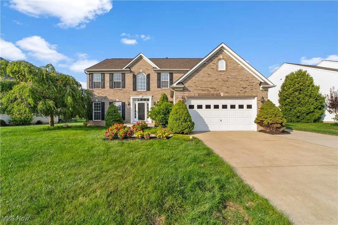 Front of home featuring mature landscaping and a wide driveway.