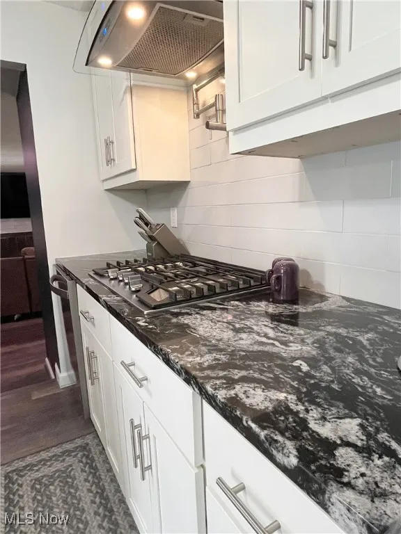 Kitchen with decorative backsplash, white cabinetry, ventilation hood, dark stone countertops, and stainless steel gas cooktop
