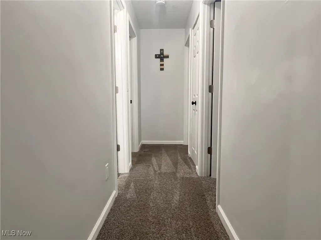 Hallway featuring baseboards and dark colored carpet