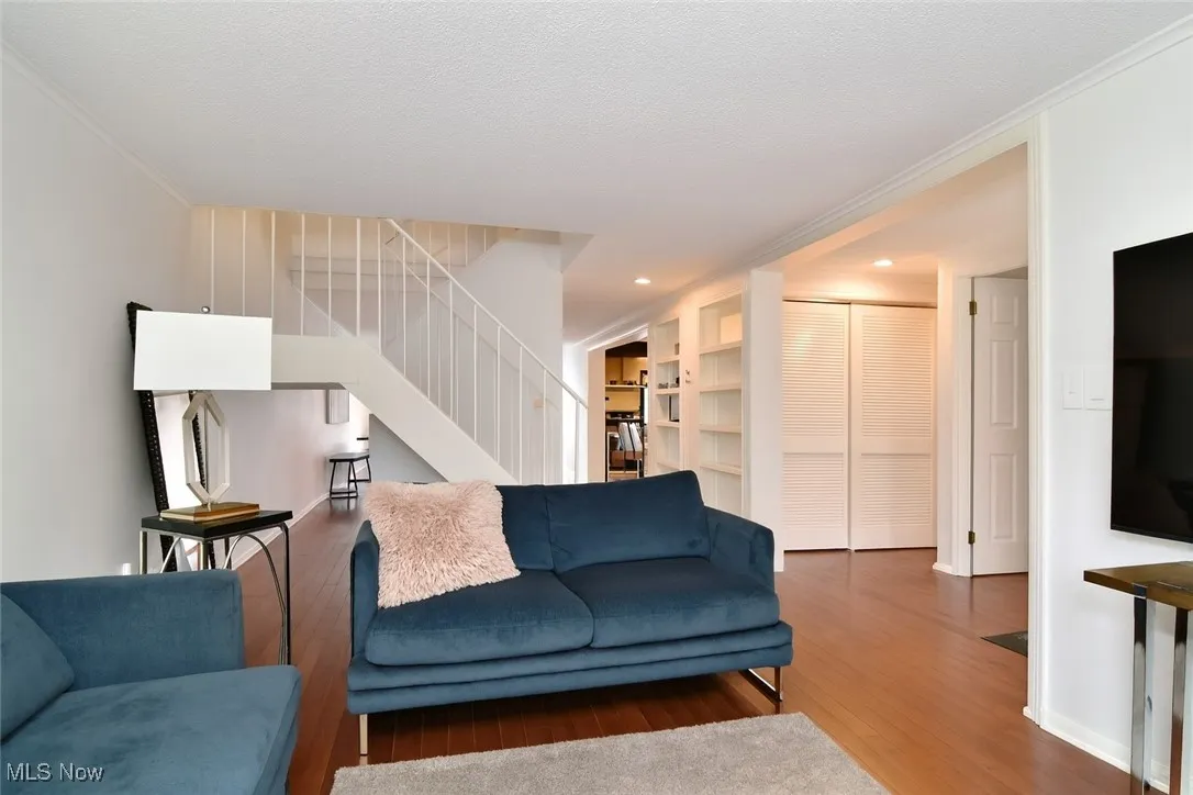 Living room with wood finished floors, built in features, stairs, crown molding, and recessed lighting
