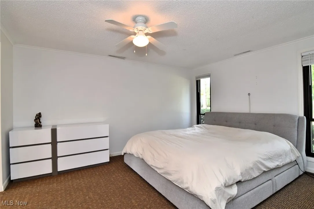 Carpeted bedroom with ornamental molding, a textured ceiling, and ceiling fan
