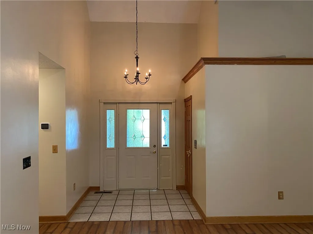 Foyer featuring light wood finished floors, a chandelier, and a towering ceiling