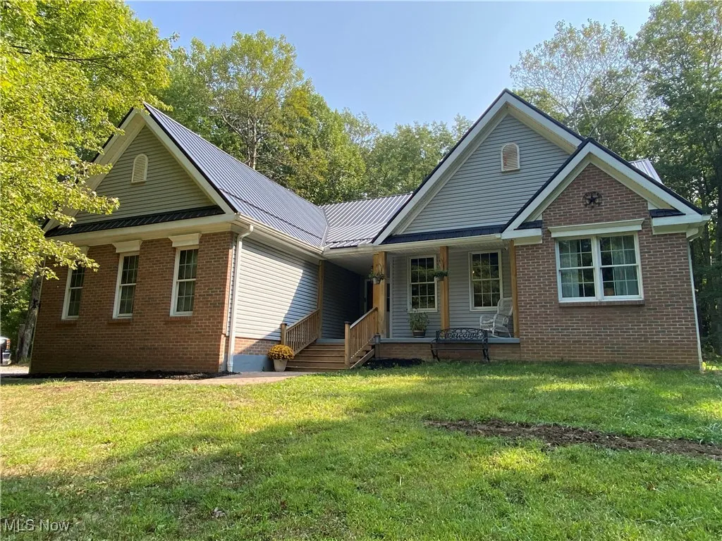 Single story home with covered porch, brick siding, a front lawn, and a metal roof
