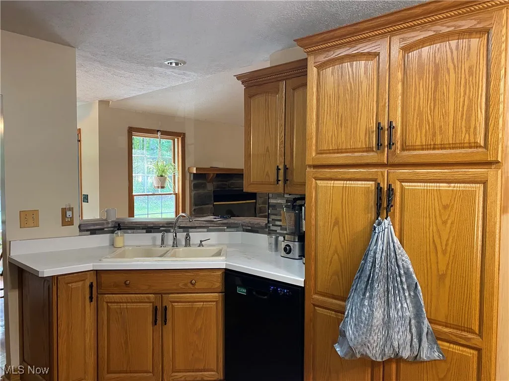 Kitchen featuring brown cabinetry, dishwasher, a textured ceiling, and light countertops