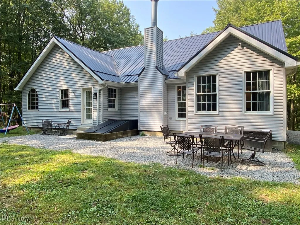 Rear view of house with a patio, a chimney, a metal roof, and a yard