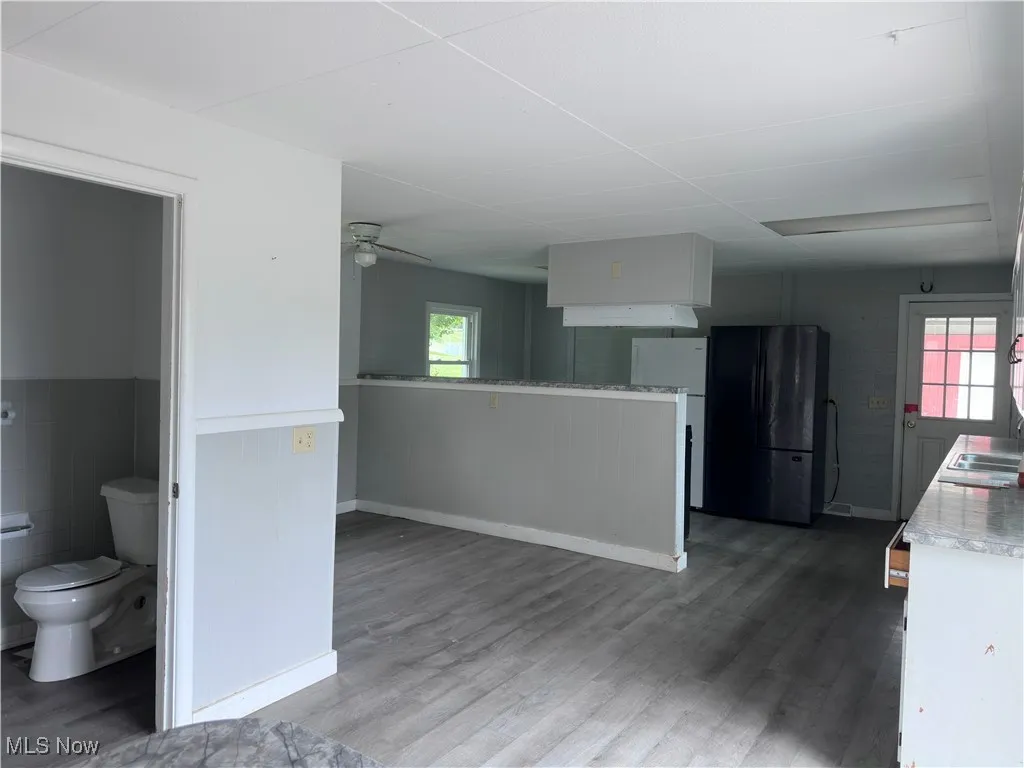 Kitchen with freestanding refrigerator, light countertops, a ceiling fan, a wainscoted wall, and light wood-style floors