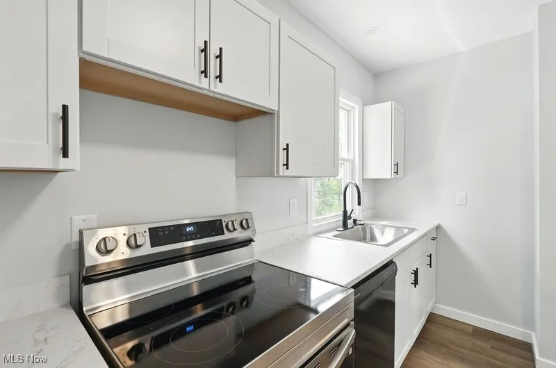 Kitchen featuring stainless steel range with electric stovetop, white cabinets, light countertops, black dishwasher, and dark wood-style flooring