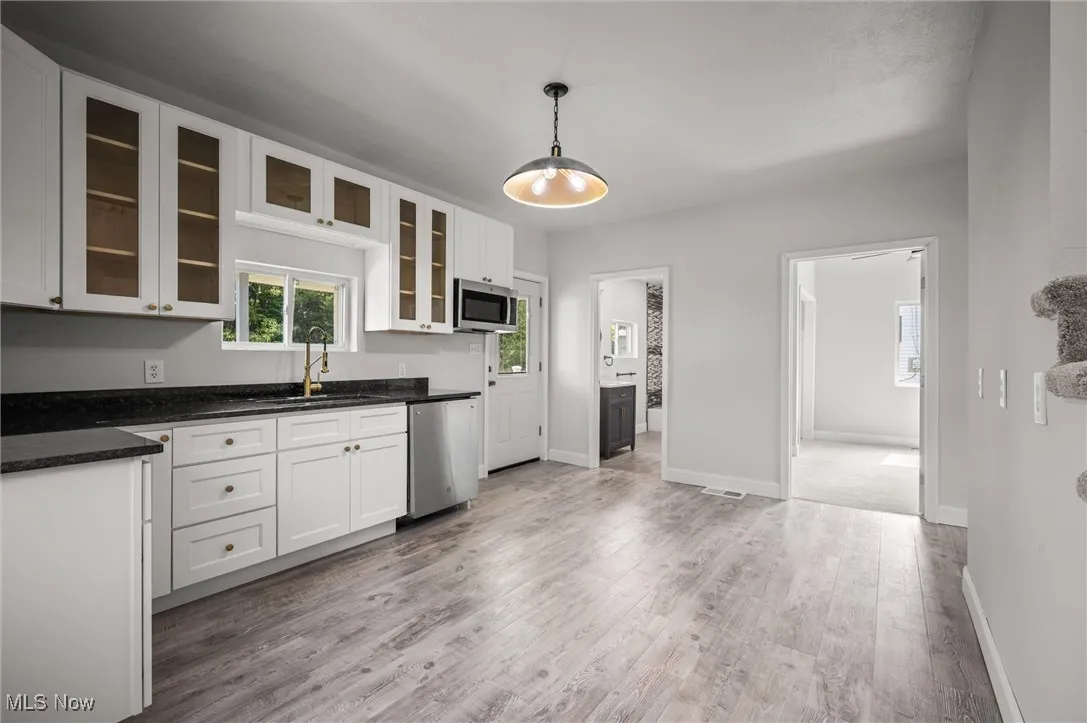 Kitchen with white cabinets, dark stone countertops, pendant lighting, glass insert cabinets, and light wood-style floors
