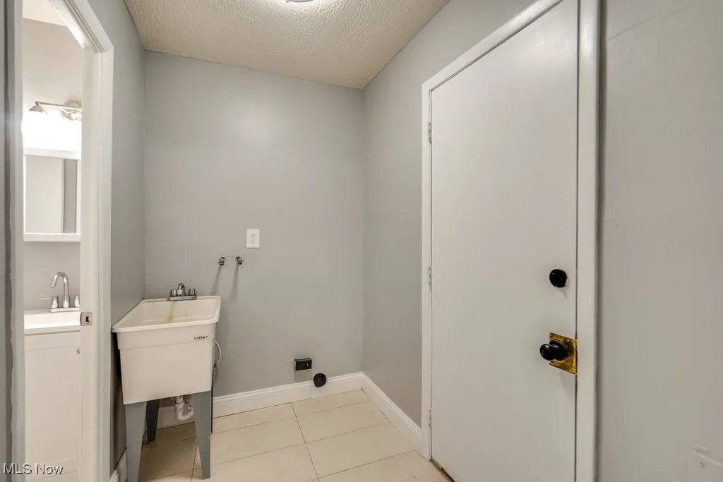 Laundry room with a textured ceiling, light tile patterned floors, and washer hookup