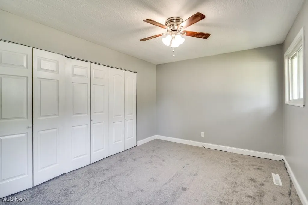 Unfurnished bedroom with light colored carpet, a closet, a ceiling fan, and a textured ceiling