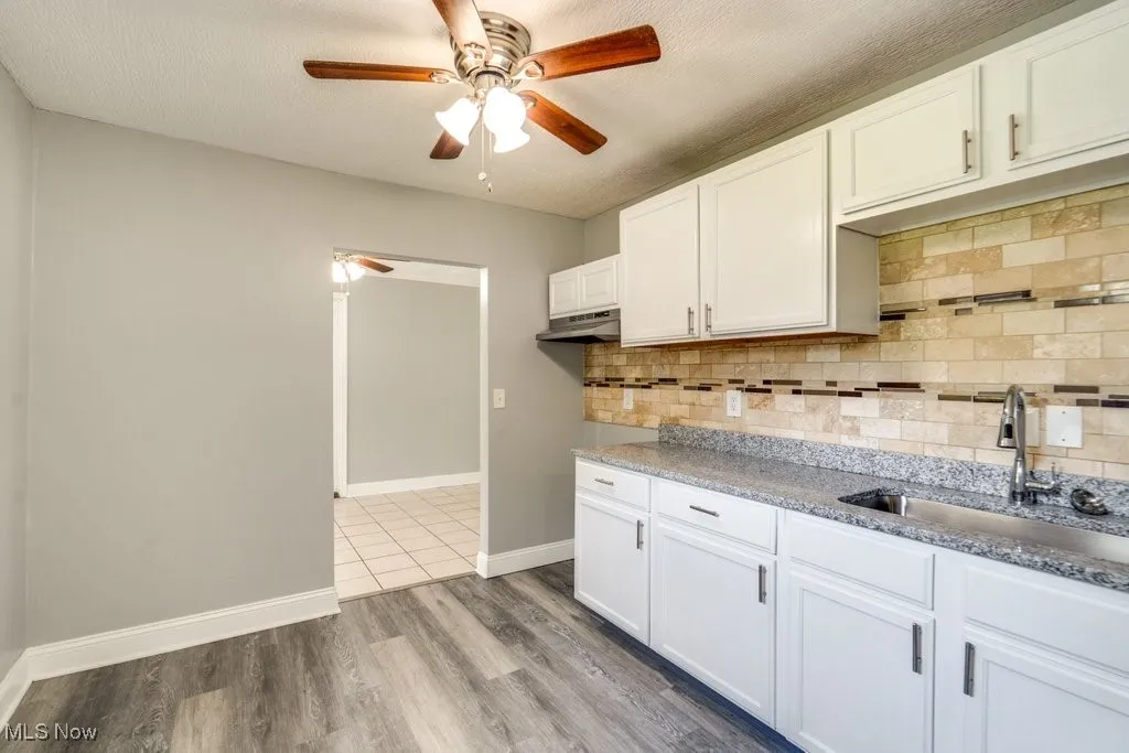 Kitchen with decorative backsplash, white cabinetry, light stone countertops, a textured ceiling, and light wood-style floors