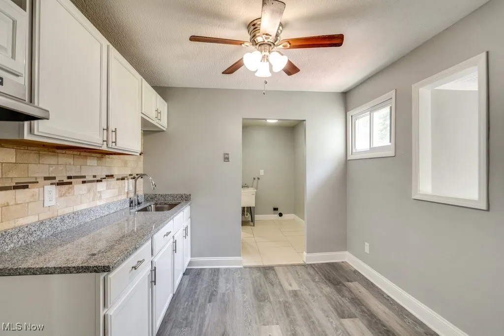 Kitchen featuring light stone countertops, white cabinetry, light wood-style floors, backsplash, and ceiling fan