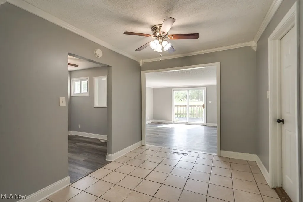 Unfurnished room with light tile patterned flooring, crown molding, a textured ceiling, and a ceiling fan