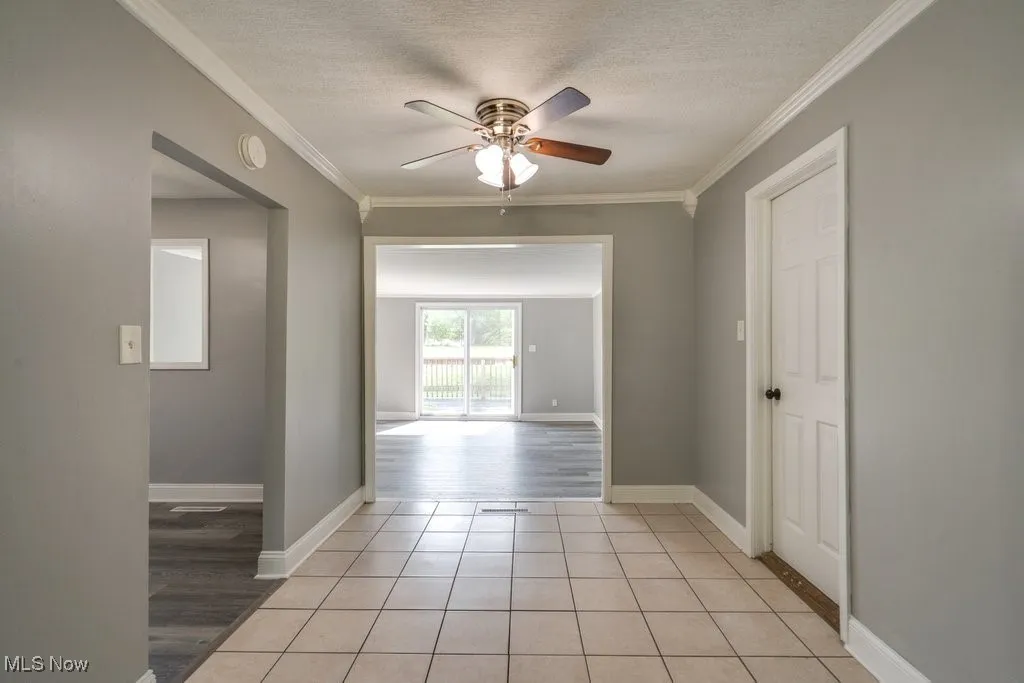Unfurnished room featuring light tile patterned flooring, a textured ceiling, ornamental molding, and a ceiling fan
