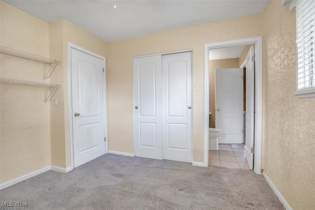 Unfurnished bedroom with a textured wall, light carpet, a closet, and light tile patterned floors