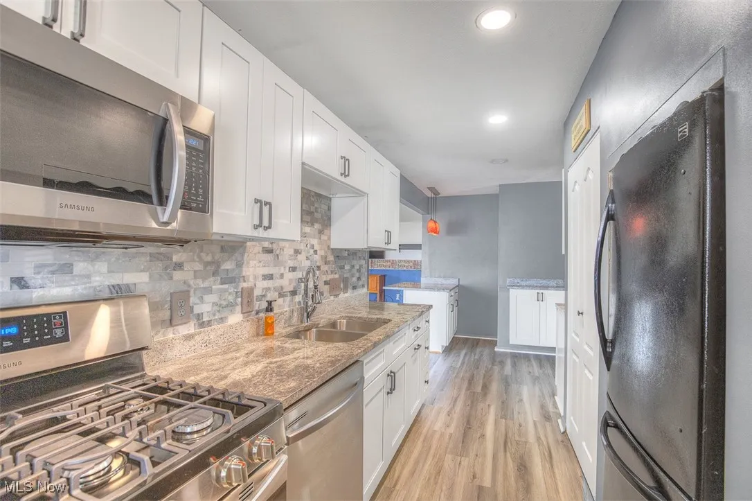 Kitchen featuring appliances with stainless steel finishes, white cabinetry, tasteful backsplash, light stone countertops, and light wood-type flooring