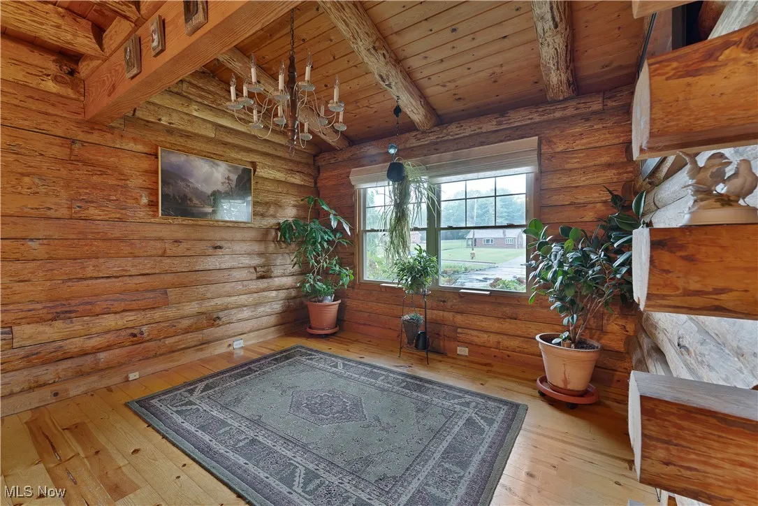 Detailed view of wood finished floors, a chandelier, log walls, and a wood ceiling with exposed beams