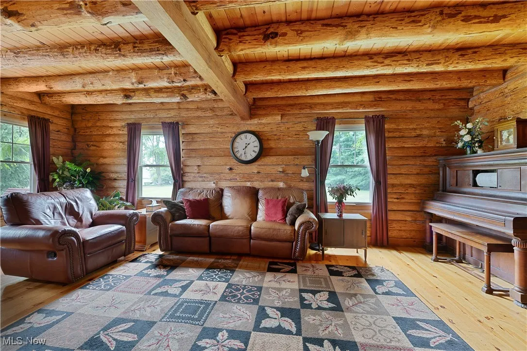 Living area featuring light wood-style flooring, plenty of natural light, rustic walls, and a wood ceiling with exposed beams