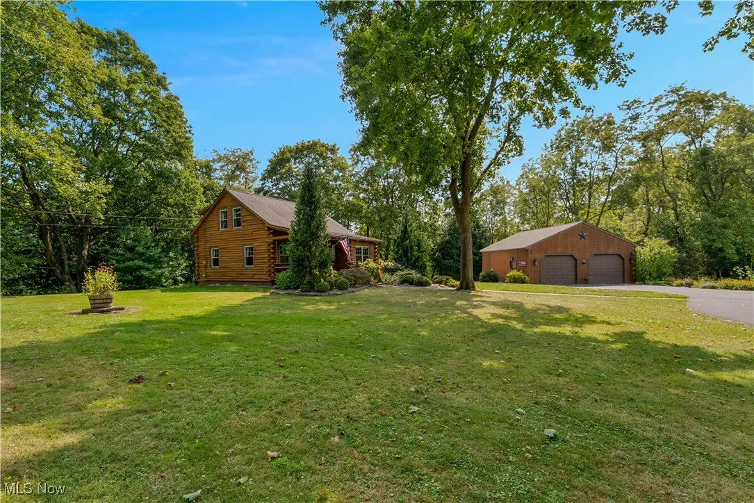 View of grassy yard with a detached garage, an outbuilding, and view of scattered trees