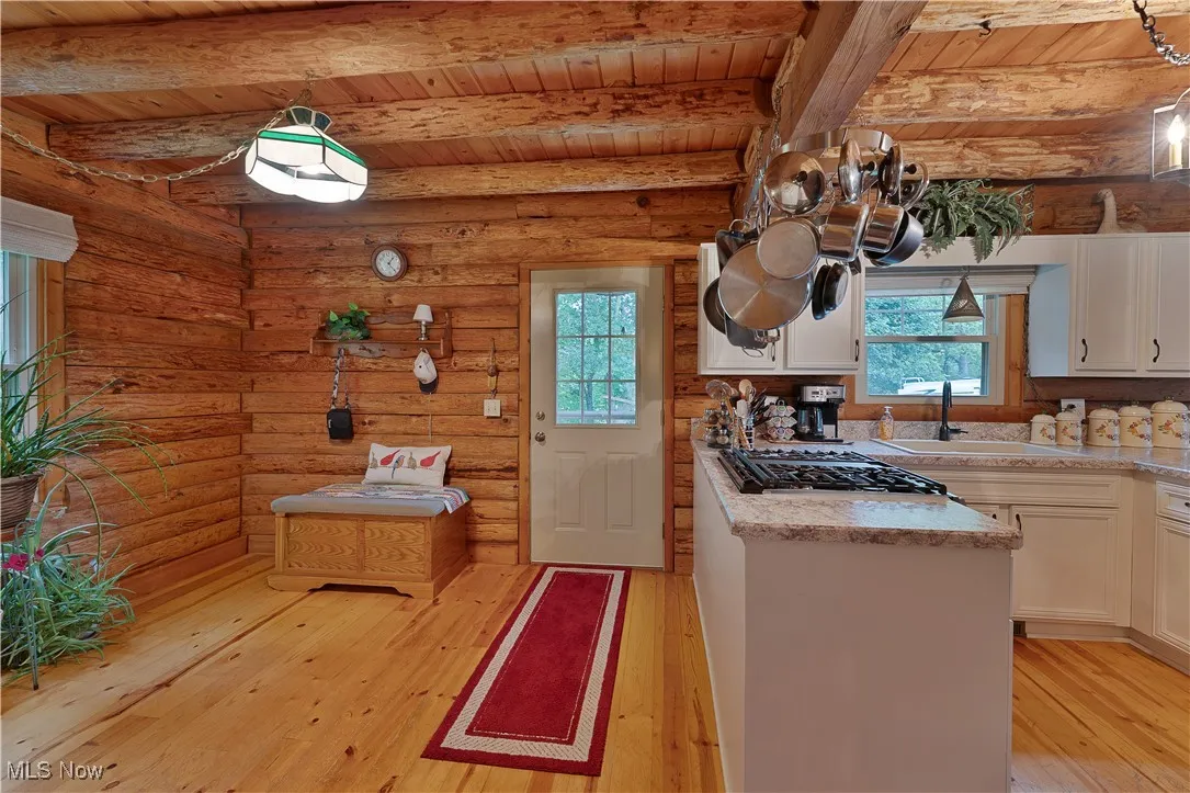 Kitchen featuring light wood-type flooring, light countertops, a wooden ceiling with exposed beams, log walls, and stainless steel gas cooktop