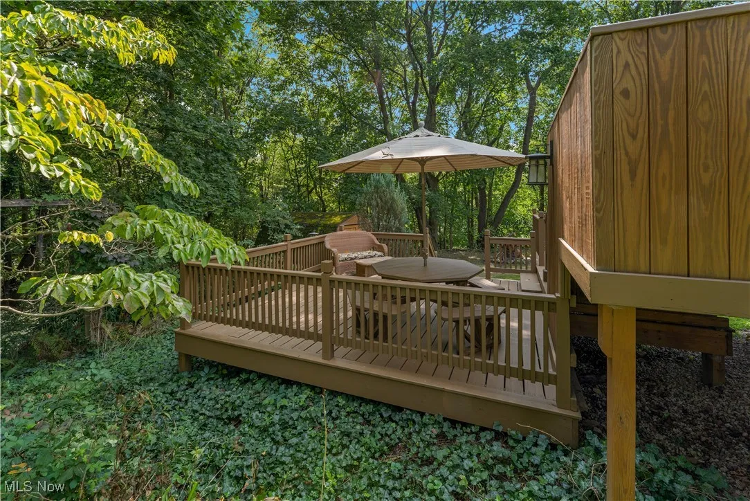 Wooden terrace featuring view of wooded area and outdoor dining space