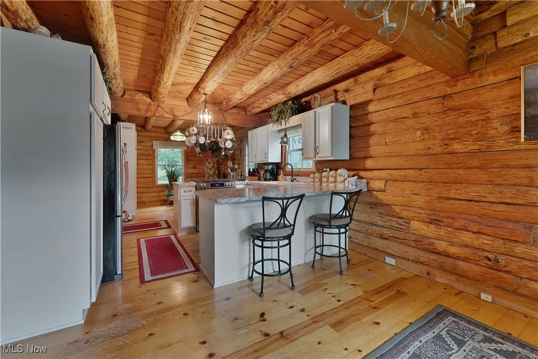 Kitchen with a chandelier, light wood-style flooring, rustic walls, white cabinetry, and a breakfast bar