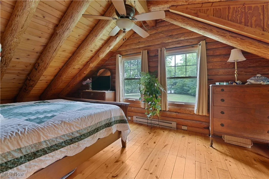 Bedroom featuring light wood-type flooring, baseboard heating, wood ceiling, ceiling fan, and rustic walls