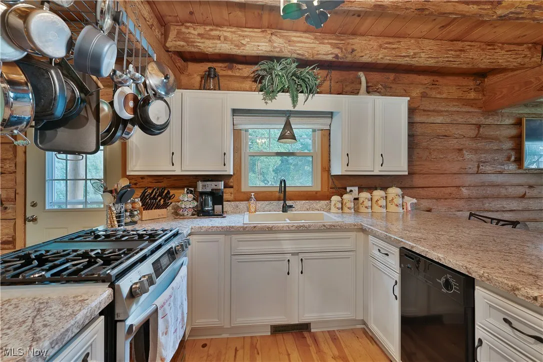 Kitchen with gas stove, white cabinets, black dishwasher, rustic walls, and light wood finished floors